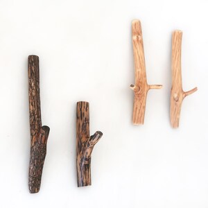 Puede incluir: Cuatro ganchos de pared con forma de ramas de &aacute;rbol. Dos ganchos son de color marr&oacute;n oscuro con una apariencia texturizada y carbonizada, mientras que los otros dos son de color tostado claro con un acabado de veta de madera natural y lisa.