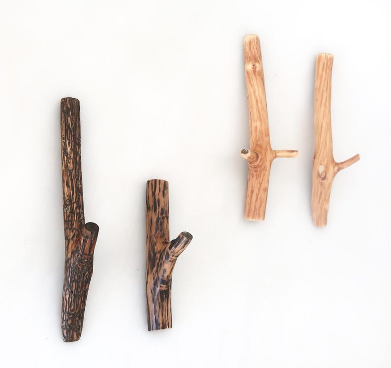 Puede incluir: Cuatro ganchos de pared con forma de ramas de &aacute;rbol. Dos ganchos son de color marr&oacute;n oscuro con una apariencia texturizada y carbonizada, mientras que los otros dos son de color tostado claro con un acabado de veta de madera natural y lisa.