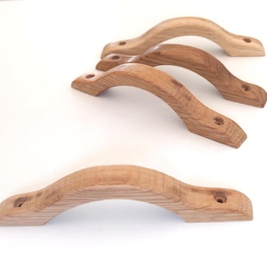 Puede incluir: Un conjunto de tiradores de madera para armarios en varios tonos marrones. Los tiradores tienen un diseño curvo y ergonómico con agujeros pretaladrados para una fácil instalación. La veta natural de la madera es visible, añadiendo un toque rústico. Cada tirador mide unos 15 cm.