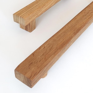 Könnte beinhalten: Zwei rechteckige Holzschrankgriffe mit natürlicher Holzmaserung. Die Griffe sind hellbraun und haben ein schlichtes, modernes Design. Ein Griff befindet sich im Vordergrund, der andere im Hintergrund. Die Griffe sind aus massivem Holz gefertigt.