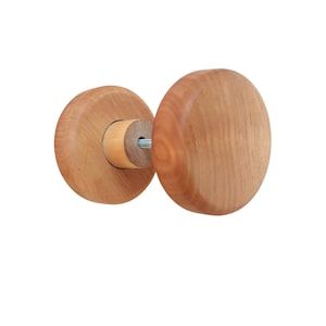 May include: A wooden door knob with a round, flat design. The knob is made of light brown wood with a natural grain pattern.