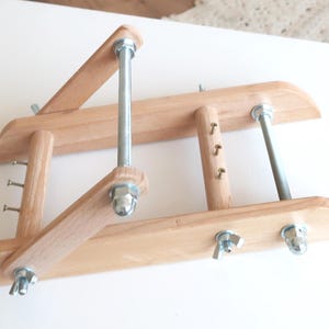 May include: A wooden embroidery hoop frame with metal hardware. The frame is made of light-colored wood and features adjustable arms and screws. The metal components include bolts, nuts, and screws, providing stability and adjustability for various embroidery projects.
