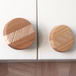 Puede incluir: Dos pomos redondos de madera con un patrón de rayas. Los pomos son de color marrón claro con rayas blancas.