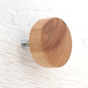 May include: A round, unfinished wooden knob with a light brown color. The knob is attached to a silver metal screw. The wood grain is visible on the surface of the knob. This is a cabinet or drawer pull.