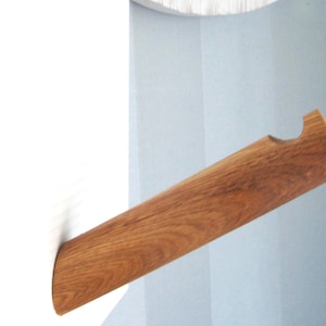 Puede incluir: Un perchero de pared de madera con un extremo redondeado y un recorte para colgar objetos. El perchero es de madera marrón claro y está montado en una pared azul claro.