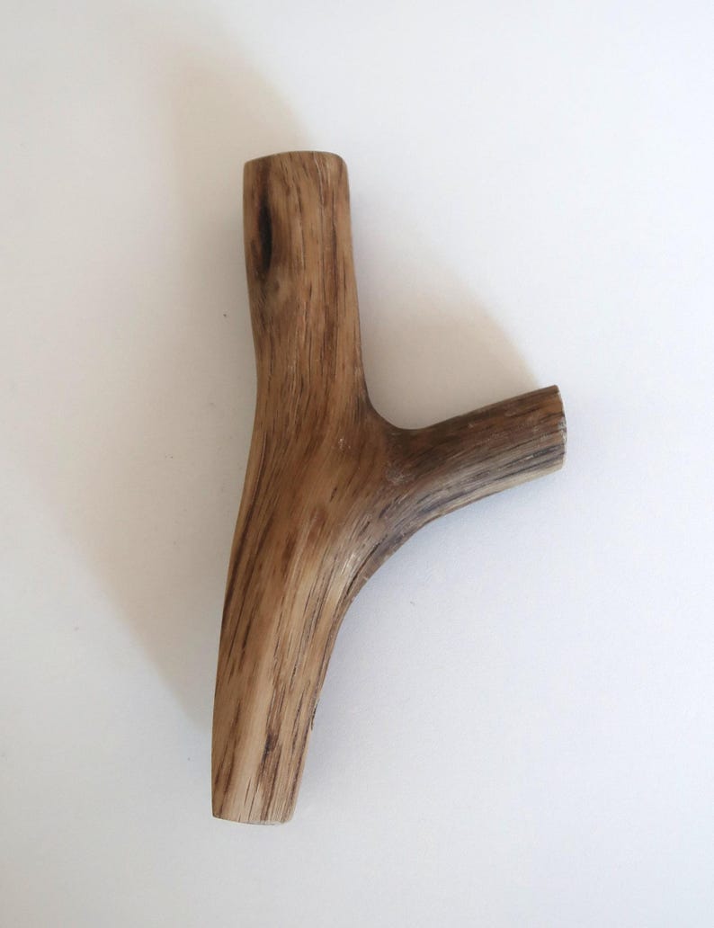 Puede incluir: Una pieza de madera natural en forma de Y con una superficie lisa y pulida. La madera presenta un color marr&oacute;n claro con vetas de color marr&oacute;n m&aacute;s oscuro que recorren verticalmente la rama, mostrando un nudo y textura distintivos.