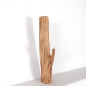 Puede incluir: Un gancho de pared de madera vertical con forma de segmento de rama de &aacute;rbol. La madera de color marr&oacute;n claro presenta vetas naturales de color marr&oacute;n oscuro y un solo pomo que sobresale en el lateral para colgar objetos. La superficie es lisa y cil&iacute;ndrica.