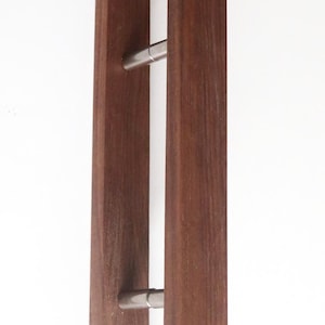 Könnte beinhalten: Ein Paar Türgriffe aus Holz mit rechteckigem Design. Die Griffe sind in einem satten Braunton gehalten und verfügen über einen Griff aus gebürstetem Metall. Die Türgriffe sind vertikal vor einem weißen Hintergrund montiert.