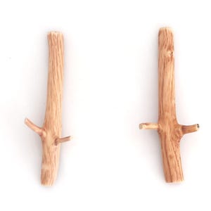 Puede incluir: Dos ganchos de pared de madera de color marr&oacute;n claro con forma de ramas de &aacute;rbol. Cada gancho presenta un tallo principal vertical con dos brazos m&aacute;s peque&ntilde;os y salientes en forma de rama a los lados, con una textura de veta de madera natural.