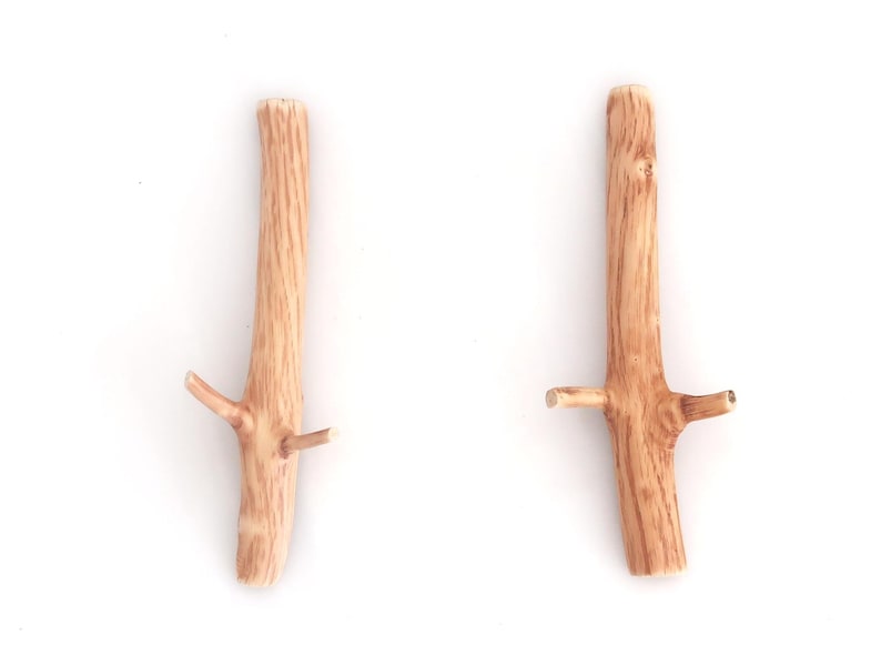 Puede incluir: Dos ganchos de pared de madera de color marr&oacute;n claro con forma de ramas de &aacute;rbol. Cada gancho presenta un tallo principal vertical con dos brazos m&aacute;s peque&ntilde;os y salientes en forma de rama a los lados, con una textura de veta de madera natural.
