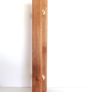 Può includere: Un portarotolo di carta igienica in legno con finitura a venatura naturale. Il supporto ha un design semplice e minimalista con due montanti verticali e un piccolo tassello rotondo per il rotolo di carta igienica. Il legno è di colore marrone chiaro.