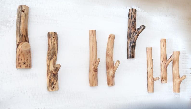 Puede incluir: Una colecci&oacute;n de siete ganchos de pared fabricados con ramas de madera natural de color marr&oacute;n claro. Cada gancho presenta una forma org&aacute;nica &uacute;nica con vetas, nudos y texturas de madera visibles, dise&ntilde;ados para colgar objetos en la pared.