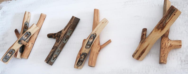 Puede incluir: Un conjunto de cuatro ganchos de pared fabricados con ramas de &aacute;rbol naturales de color marr&oacute;n claro. Cada gancho presenta una superficie de madera pulida y lisa con vetas visibles y placas de montaje met&aacute;licas integradas con ranuras.