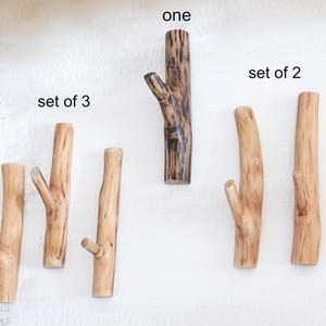 Puede incluir: Una colecci&oacute;n de ganchos de pared de madera con forma de ramas de &aacute;rbol. El juego de 3 presenta madera de color marr&oacute;n claro, el gancho individual es marr&oacute;n oscuro con vetas negras y el juego de 2 consta de ganchos de madera clara con vetas.