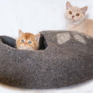 May include: Two orange tabby kittens, one inside a grey felt cat bed and the other sitting on the edge of the bed. The bed is shaped like a shoe.