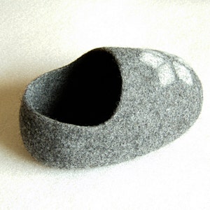 May include: A grey felt slipper with a white flower design. The slipper is made of soft, fuzzy material and has a rounded shape.