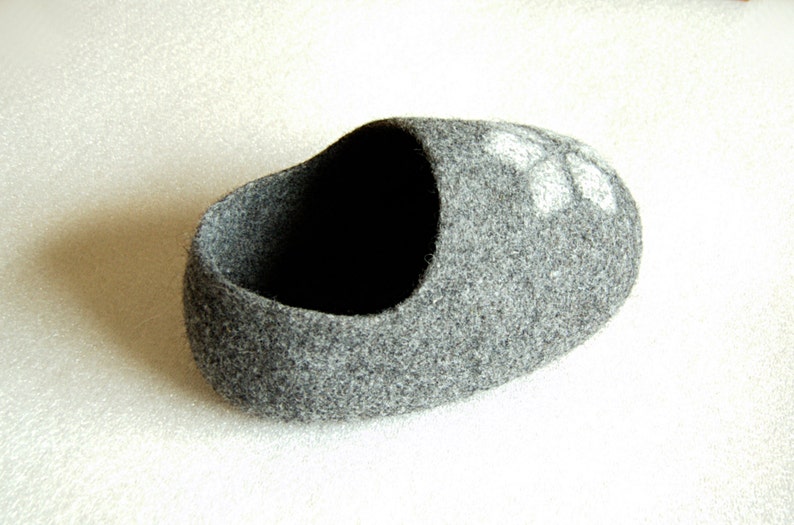 May include: A grey felt slipper with a white flower design. The slipper is made of soft, fuzzy material and has a rounded shape.