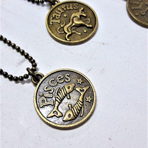 May include: Two gold-toned zodiac necklaces with black chains. The necklaces feature a circular pendant with the zodiac signs Taurus and Pisces.