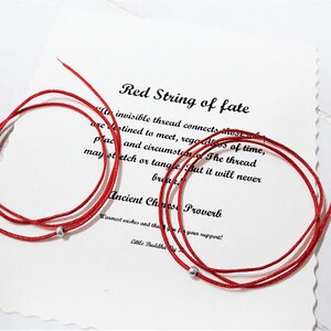 Op de afbeelding: Rood draad van het lot armband met zilveren kralen. De armband ligt op een witte achtergrond met een citaat over de rode draad van het lot. "Een onzichtbare draad verbindt degenen die bestemd zijn om elkaar te ontmoeten, ongeacht tijd, plaats en omstandigheden. De draad kan uitrekken of verstrengelen, maar hij zal nooit breken. Oud Chinees spreekwoord."