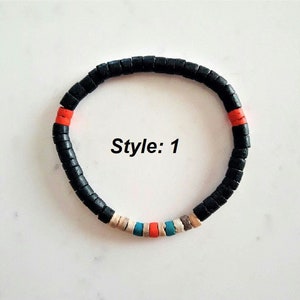Pode incluir: Uma pulseira circular composta por pequenas contas cil&iacute;ndricas de cor preta mate. O design apresenta duas contas cor de laranja, uma conta azul brilhante, uma conta bege e uma conta cinzenta intercaladas entre as pretas. O texto Style: 1 &eacute; vis&iacute;vel.