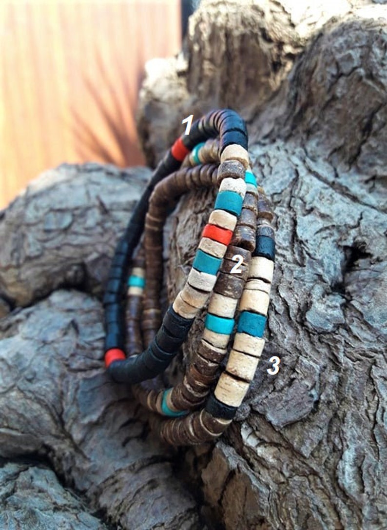 Pode incluir: Tr&ecirc;s pulseiras feitas de pequenas contas planas e circulares nas cores preta, castanha, bege, turquesa e vermelha. As pulseiras est&atilde;o numeradas 1, 2 e 3, com padr&otilde;es de cores alternados de contas com aspeto de madeira e acabamento mate.