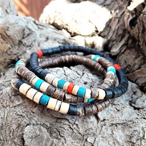 Pode incluir: Um conjunto de tr&ecirc;s pulseiras empilhadas feitas de pequenas contas cil&iacute;ndricas em forma de disco. As contas apresentam uma paleta de cores preto fosco, bege natural, turquesa brilhante e vermelho vibrante, dispostas em padr&otilde;es alternados.