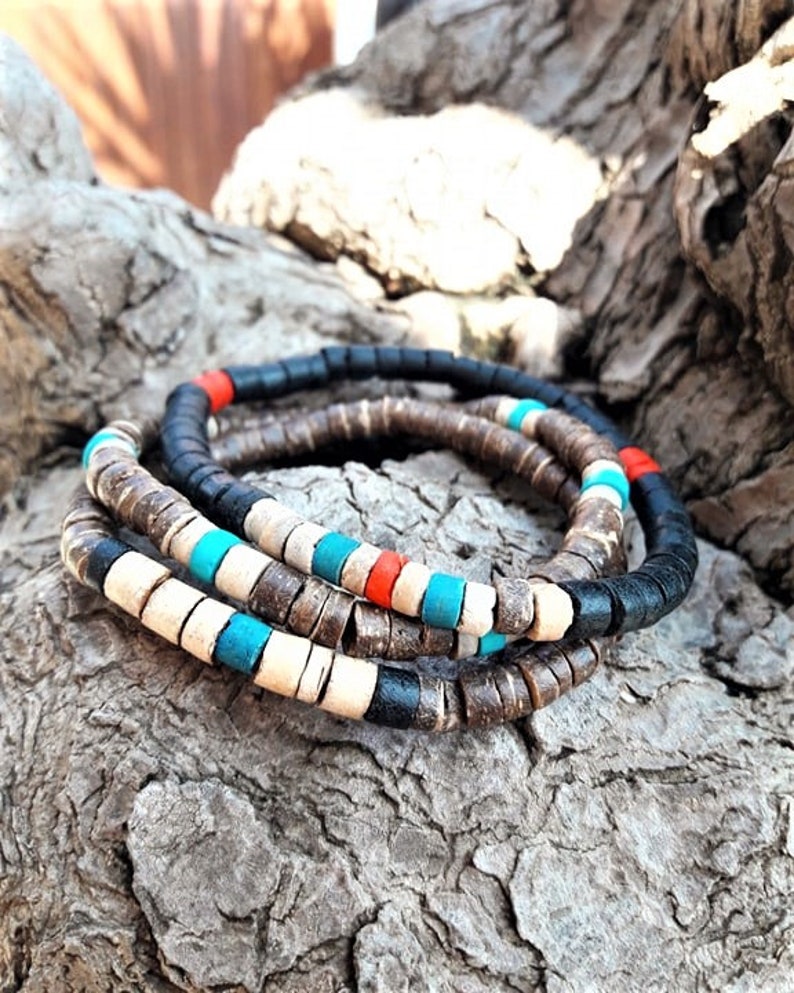 Pode incluir: Um conjunto de tr&ecirc;s pulseiras empilhadas feitas de pequenas contas cil&iacute;ndricas em forma de disco. As contas apresentam uma paleta de cores preto fosco, bege natural, turquesa brilhante e vermelho vibrante, dispostas em padr&otilde;es alternados.