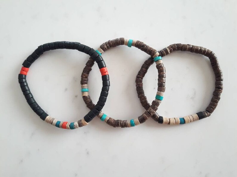 Pode incluir: Tr&ecirc;s pulseiras circulares feitas de pequenas contas planas em forma de disco. A primeira &eacute; principalmente preta com detalhes em vermelho, turquesa e bege. A segunda e a terceira s&atilde;o castanhas com contas turquesa e bege intercaladas.