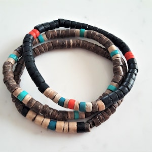 Pode incluir: Uma pulseira de v&aacute;rias voltas composta por pequenas contas cil&iacute;ndricas em forma de disco em preto mate, castanho escuro, bege claro, turquesa brilhante e laranja vibrante. As contas est&atilde;o dispostas em padr&otilde;es repetidos nos fios.