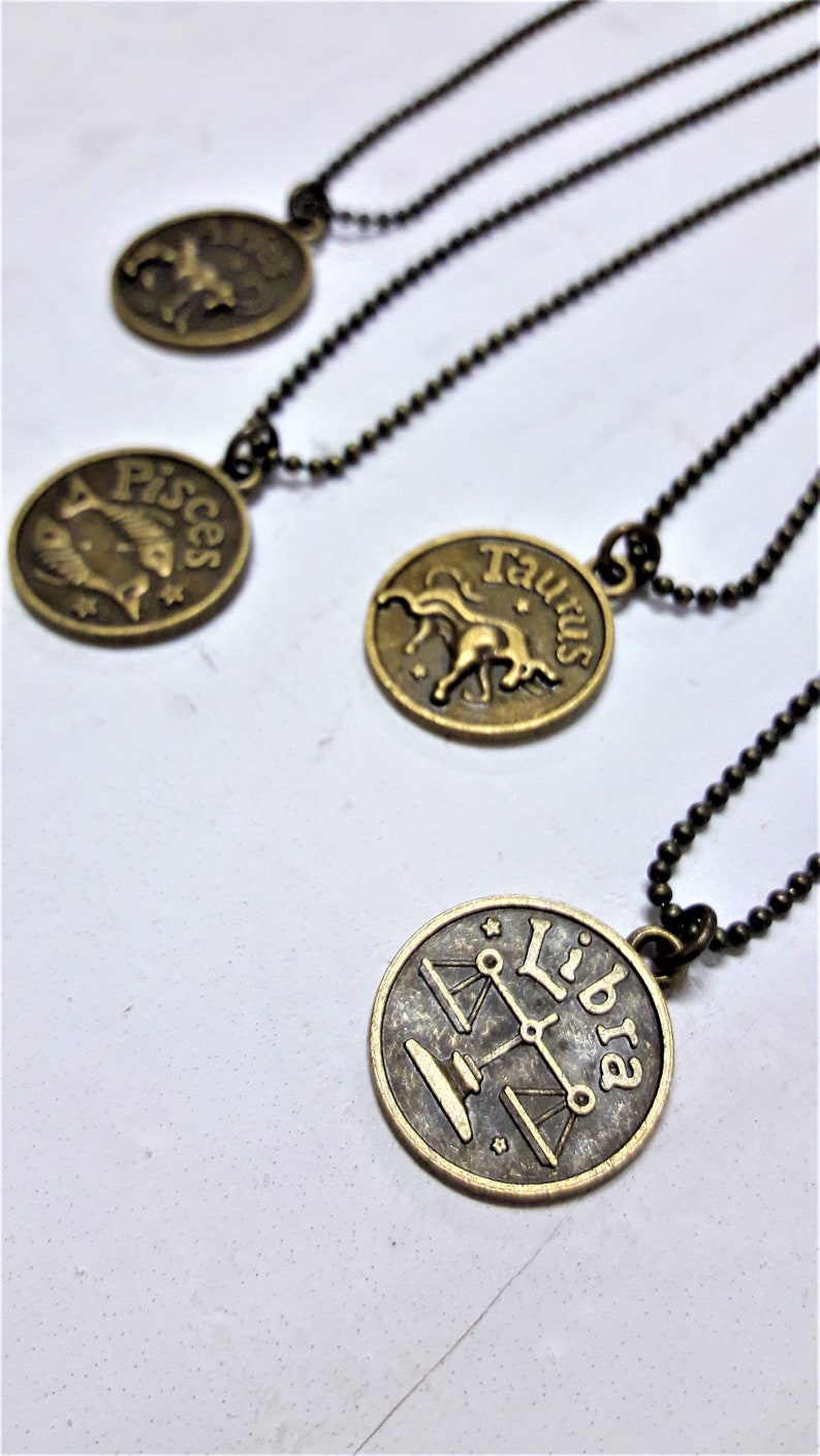 May include: Four gold-toned necklaces with zodiac signs as pendants. The signs are Pisces, Taurus, Libra, and an unknown sign.