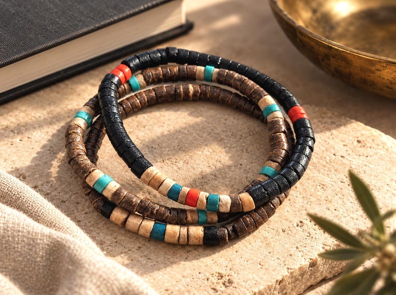 Pode incluir: Um conjunto de tr&ecirc;s pulseiras empilhadas feitas de pequenas contas cil&iacute;ndricas em forma de disco. As contas s&atilde;o coloridas em preto, castanho escuro, bege claro, turquesa brilhante e laranja vibrante, dispostas em padr&otilde;es alternados ao longo de cada fio.