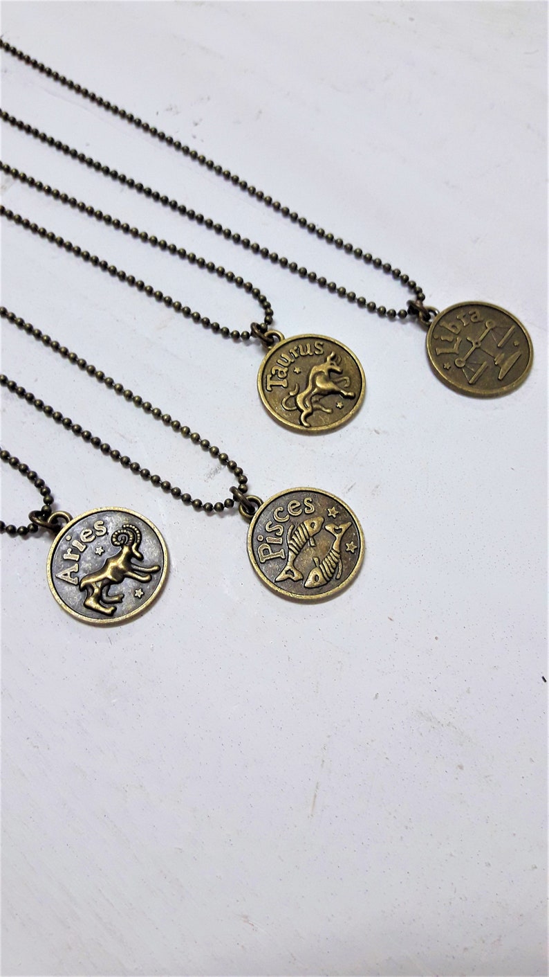 May include: Four gold-toned zodiac necklaces with chain links. The necklaces feature pendants with the astrological signs of Aries, Taurus, Pisces, and Libra.