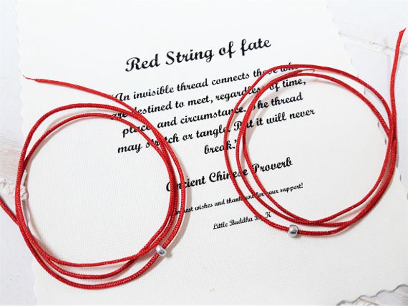 Op de afbeelding: Twee rode draden van het lot met zilveren kralen, aan elkaar gebonden. De draden liggen op een witte achtergrond met tekst die "Red String of fate" en "Een onzichtbare draad verbindt degenen die bestemd zijn om elkaar te ontmoeten, ongeacht tijd, plaats en omstandigheden. De draad kan uitrekken of in de knoop raken, maar hij zal nooit breken."  "Oud Chinees spreekwoord" luidt.
