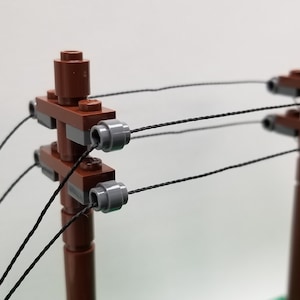 May include: A close-up of a brown wooden Lego model of a power pole with gray insulators and black wires.