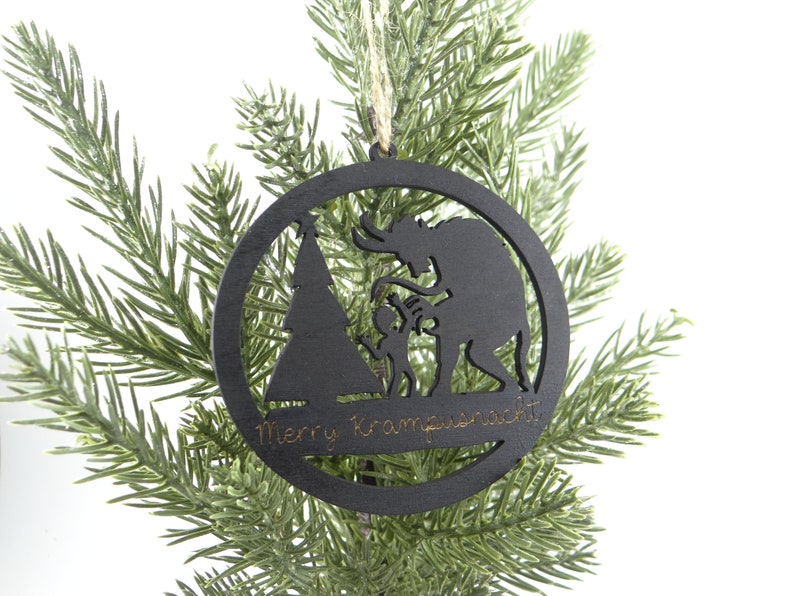 May include: Black wooden Christmas ornament with a silhouette of Krampus, a Christmas demon, and a child. The ornament is round and has the text "Merry Krampusnacht" inscribed on the bottom.