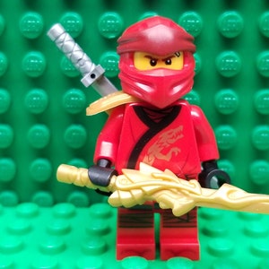 May include: Red Lego minifigure with a red and black ninja outfit, holding a gold sword and a silver sword on his back. The minifigure has a red mask with a black dragon design on the chest.