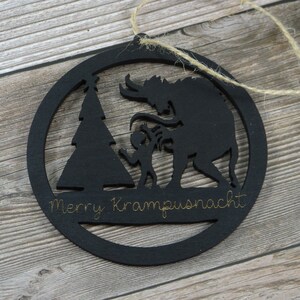May include: Black wooden Christmas ornament with a silhouette of a Krampus, a Christmas tree, and a child. The ornament has the text "Merry Krampusnacht" written on it.