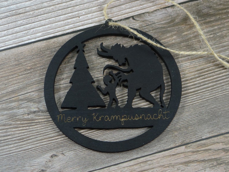 May include: Black wooden Christmas ornament with a silhouette of a Krampus, a Christmas tree, and a child. The ornament has the text "Merry Krampusnacht" written on it.