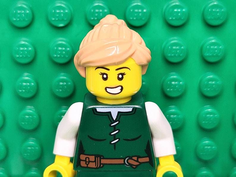 May include: A Lego minifigure with blonde hair, a green shirt, a brown belt, and a white collar. The minifigure is smiling and has a yellow face.
