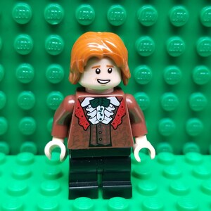 May include: A Lego minifigure with brown hair, a brown shirt with red and white details, a green bow tie, and black pants.
