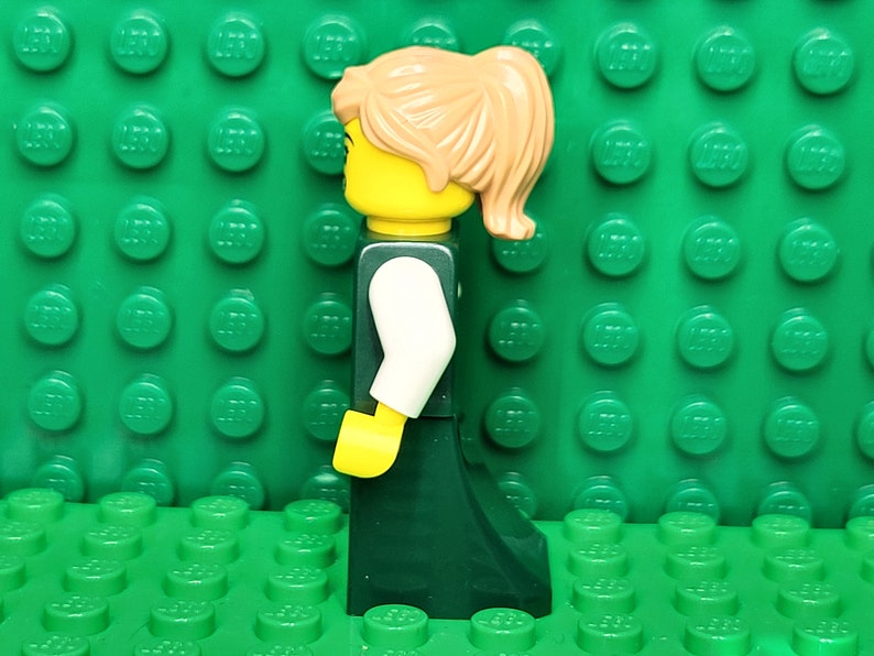 May include: A Lego minifigure of a woman with brown hair in a ponytail, wearing a white shirt and a dark green skirt.
