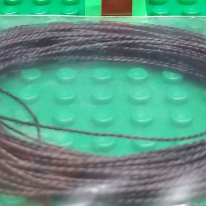 May include: A close-up of a spool of dark brown and black thread. The thread is wound tightly around the spool and is ready to be used for sewing or crafting.