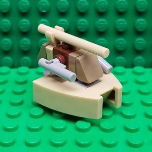May include: A small, beige and brown Lego spaceship with a gray gun and a tan cannon. The spaceship is sitting on a green Lego baseplate.