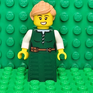 May include: A green and white LEGO minifigure of a woman with brown hair, a brown belt, and a smiling face.