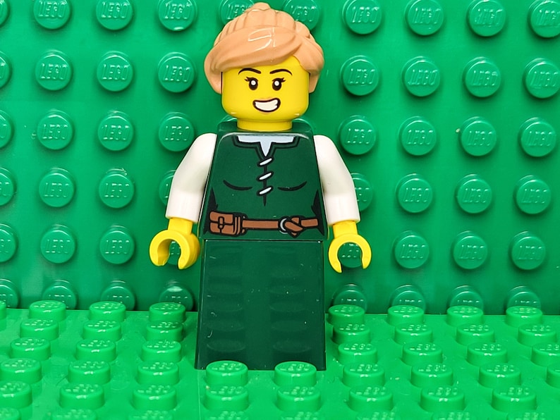 May include: A green and white LEGO minifigure of a woman with brown hair, a brown belt, and a smiling face.