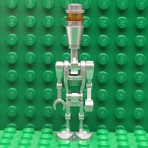 May include: A silver and orange Lego minifigure of a droid with a tool in its hand.