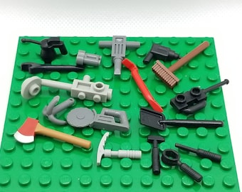 May include: A collection of 14 gray, black, and red LEGO tools, including a jackhammer, a saw, a shovel, a pickaxe, a wrench, a hammer, a broom, and an axe. The tools are arranged on a green LEGO baseplate.