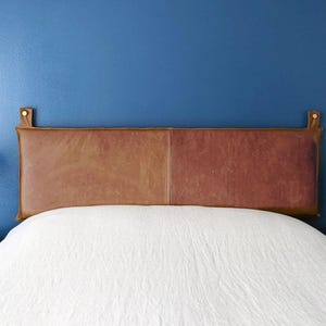 May include: A white bed with a brown leather headboard against a blue wall. Two white table lamps with round shades are on nightstands on either side of the bed.