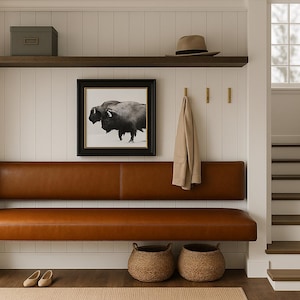 Puede incluir: Entrada de casa con un banco de cuero marrón, una impresión enmarcada de bisonte en blanco y negro y una estantería de madera. Un abrigo cuelga de la pared y dos cestas tejidas se colocan debajo del banco. La escalera es visible en el fondo.