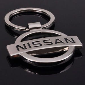 May include: Silver key ring with a black Nissan logo. The logo is a circle with the word "NISSAN" in black letters.